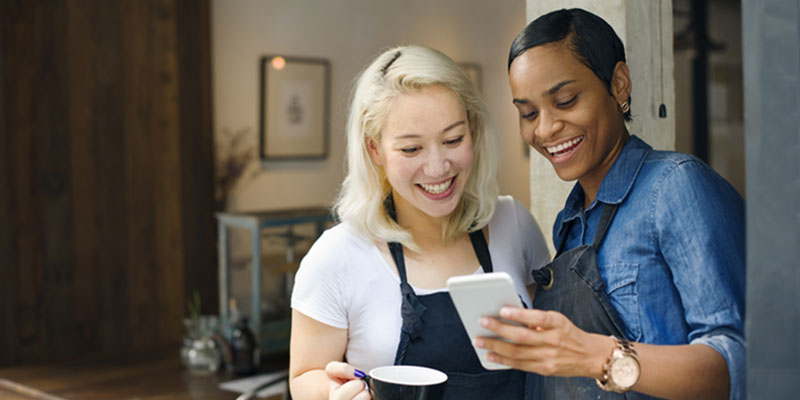 Two business people in aprons looking at a cell phone